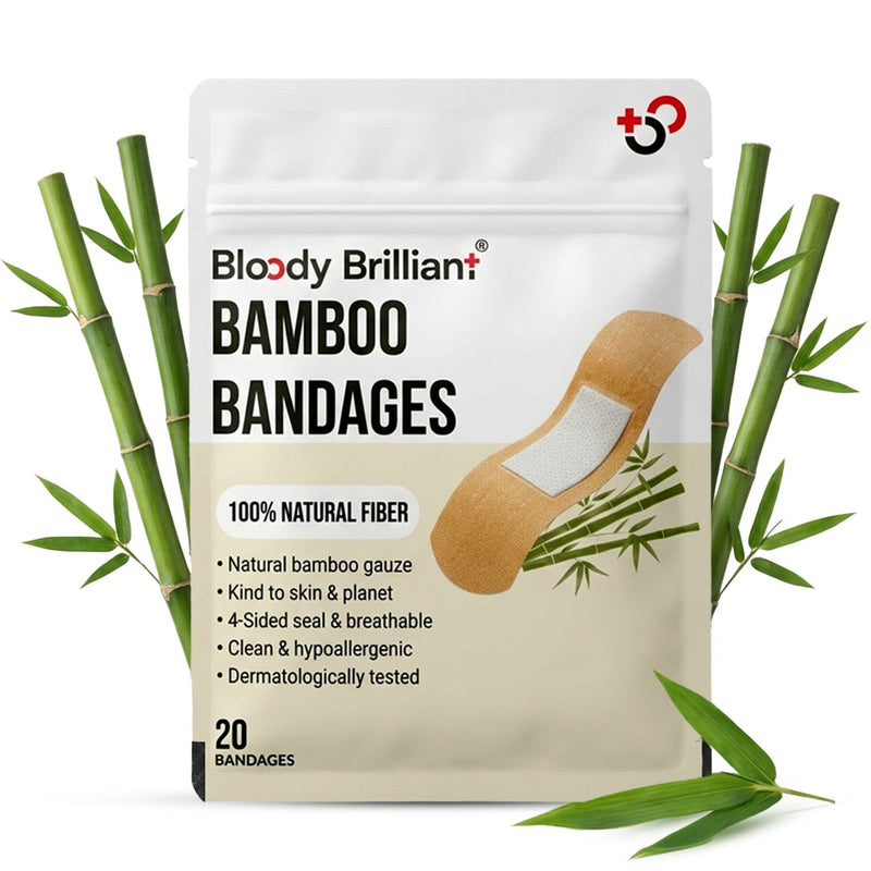 A stand-up pouch of Bloody Brilliant Bamboo Bandages surrounded by decorative green bamboo stalks and leaves on a white background. The pouch is white and beige with black text and shows a graphic of a beige bandage with a white center.